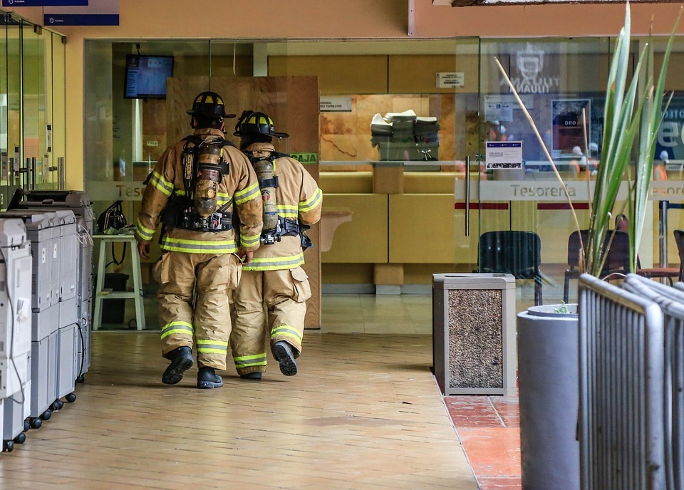 two firemen in yellow suit, cream-colored building with glass doors, steel barricades