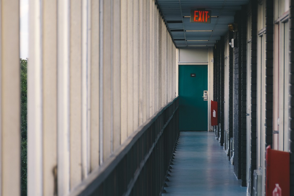 long hallway, dark green door in the middle, EXIT signage hanging