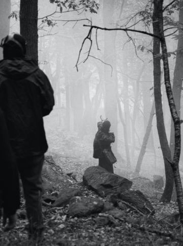 grayscale-photo-of-2-person-standing-on-rock-near-bare-trees