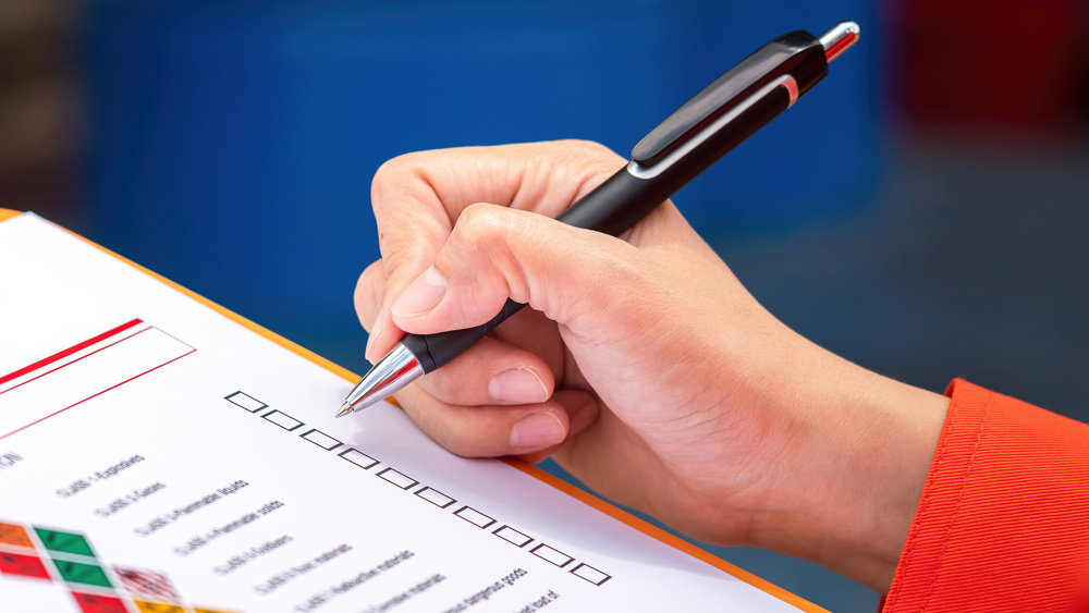 A safety engineer is using pen to rating the health risk assessment level of chemical hazardous material in the paperwork form. Industrial safety working scene, close-up and selective focus
