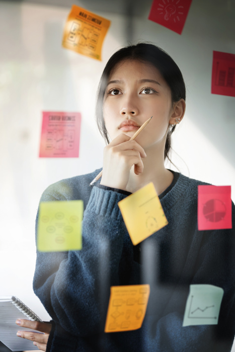 Young businesswoman thinking and planning business strategy using using post it notes on glass wall to development grow to success